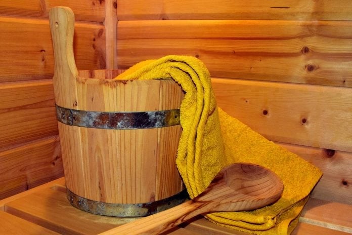 drevený kýbel s drevenou varechou a uterákom položený na dreve v saune
